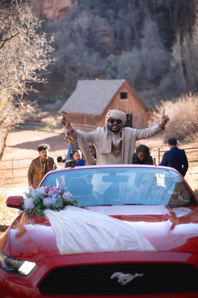 The groom arrives standing on a vintage convertible