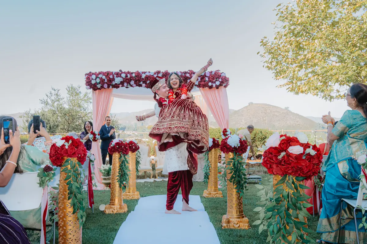 The bride, arms raised in joy, under the mandap
